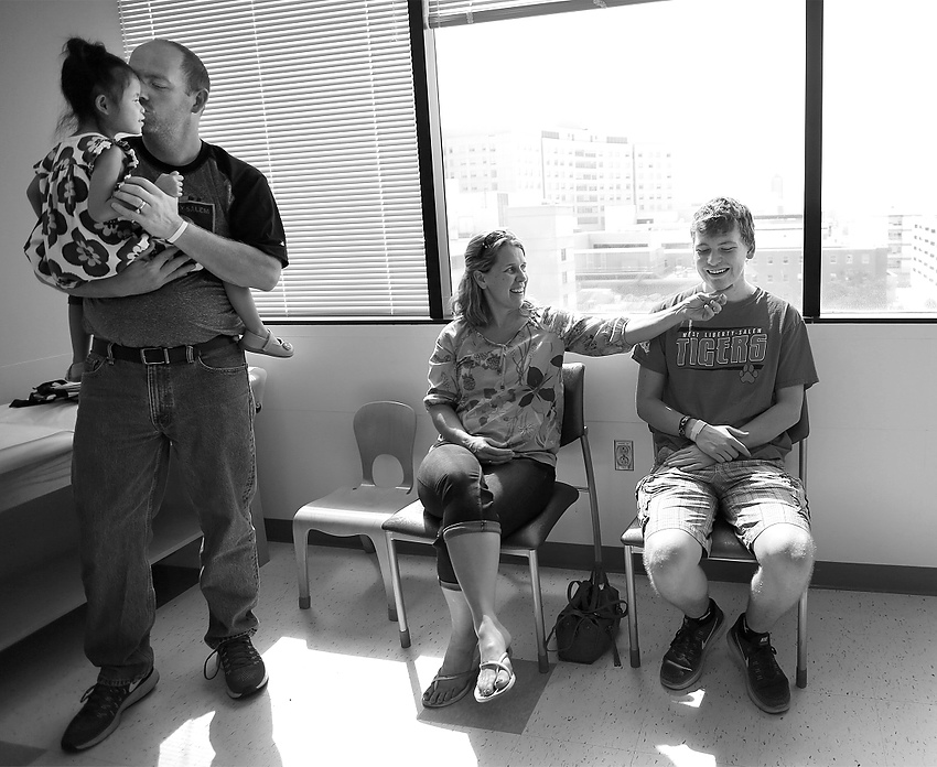Second Place, Feature Picture Story - Jonathan Quilter / The Columbus DispatchLogan smiles with his mom Julie after getting his neck and back brace removed during a doctor's appointment 3 months after the shooting. His dad, Ryan, holds daughter Shiloh, 4, during the appointment. 