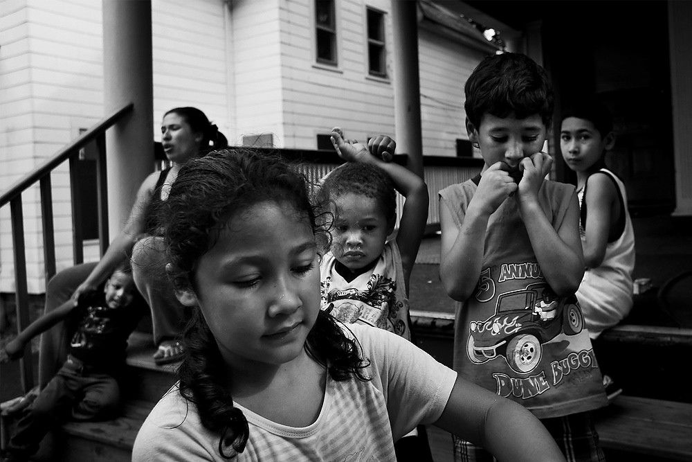 First Place, News Picture Story - Katie Rausch / The BladeSiblings, from front left, Adelisse, 6, Yadier, 3, Joseph, 5, and Gilberto, 8, play together as their mother Yadelis Lopez, back left, keeps an eye on them at their home in Rochester, New York. Ms. Lopez moved to Rochester six years ago and has rented in the city ever since. Her son, Joseph, 5, tested positive for lead at one rental property, though the family has since moved to a house that was cleared by the city. In 2005 the city of Rochester adopted legislation to aggressively lower the number of children exposed to lead in rental housing. Their law is the basis for Toledo's new lead ordinance, which requires rental buildings built before 1978 with up to four units and day-care centers to be certified “lead-safe.” 