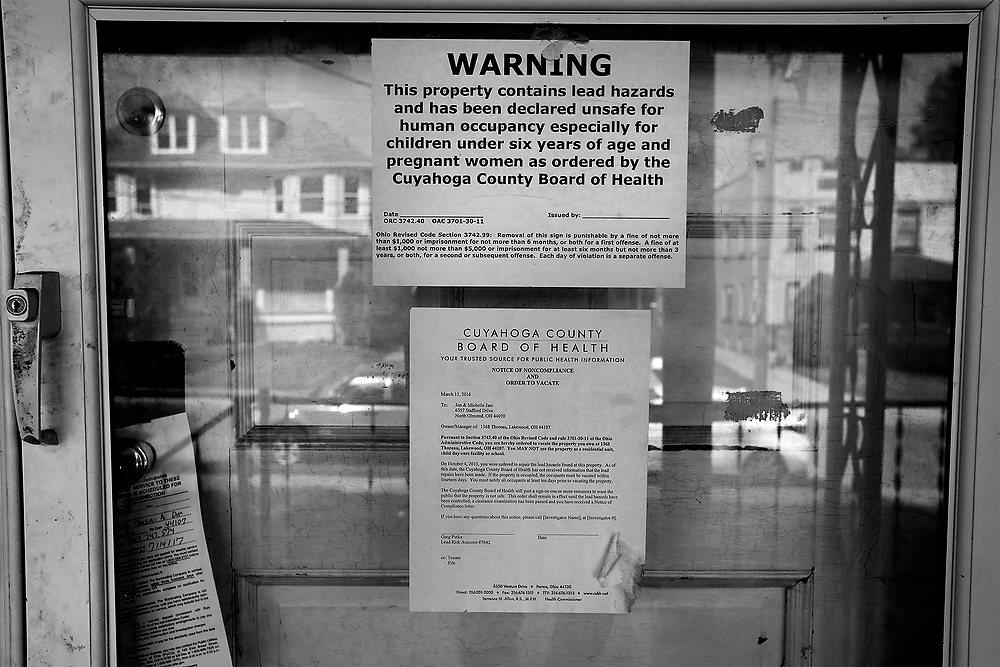 First Place, News Picture Story - Katie Rausch / The BladeA neighborhood is reflected from the porch of a house with a posted Order of Eviction in Cleveland. County boards of health can order homes vacated if the owners don't abate the lead contamination. While proponents say the laws force compliance, many neighborhoods are left with empty and blighted properties. 